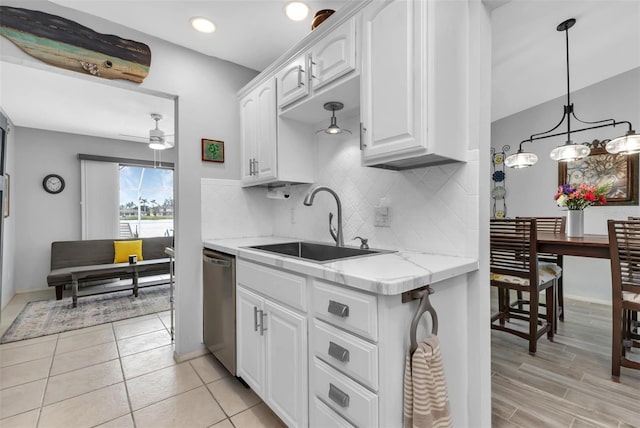 kitchen with light stone countertops, white cabinetry, stainless steel dishwasher, sink, and decorative light fixtures