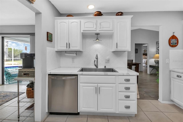 kitchen with white cabinets, stainless steel dishwasher, sink, backsplash, and light tile patterned floors