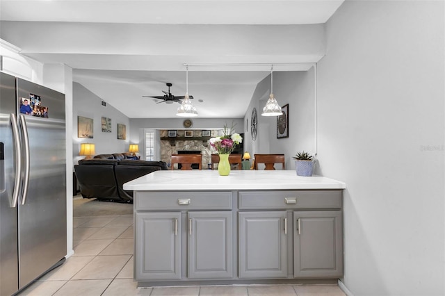 kitchen with a stone fireplace, light tile patterned floors, gray cabinets, and stainless steel fridge