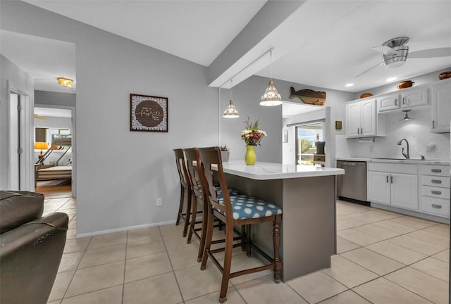 kitchen with light tile patterned floors, stainless steel dishwasher, white cabinets, sink, and a breakfast bar area