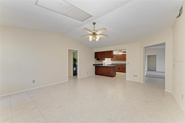 unfurnished living room featuring lofted ceiling, sink, light tile patterned floors, ceiling fan, and a textured ceiling