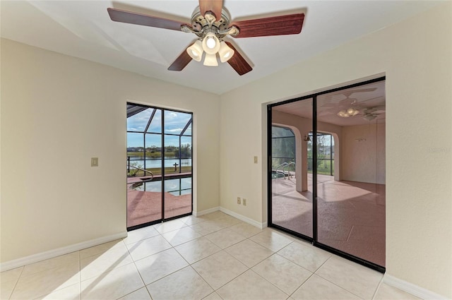 tiled empty room with a water view, ceiling fan, and a healthy amount of sunlight