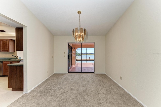 unfurnished dining area with baseboards, an inviting chandelier, light colored carpet, and a sink