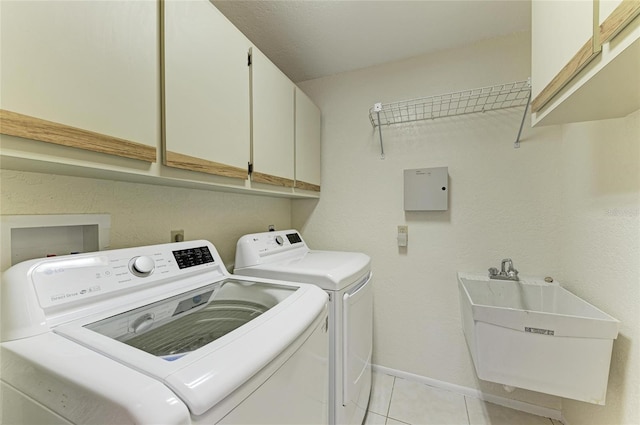 washroom featuring washing machine and clothes dryer, a sink, light tile patterned floors, cabinet space, and baseboards