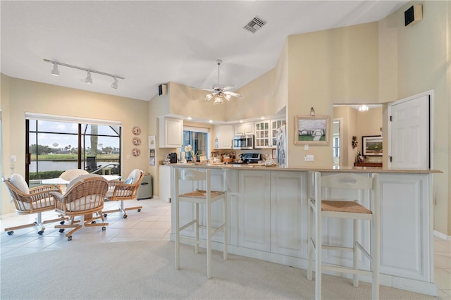 kitchen featuring a kitchen bar, white cabinetry, a water view, high vaulted ceiling, and light tile patterned floors