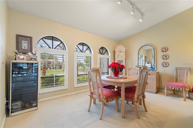 dining room featuring light carpet, vaulted ceiling, and rail lighting