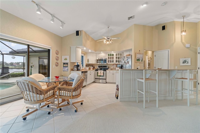 dining room with light tile patterned flooring, rail lighting, ceiling fan, and high vaulted ceiling