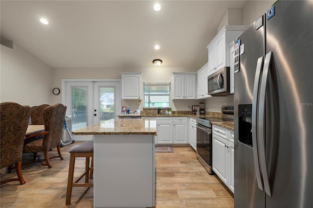 kitchen with french doors, a center island, appliances with stainless steel finishes, light stone countertops, and white cabinets