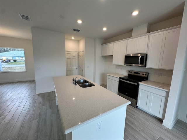 kitchen with stainless steel appliances, a kitchen island with sink, a sink, and white cabinetry