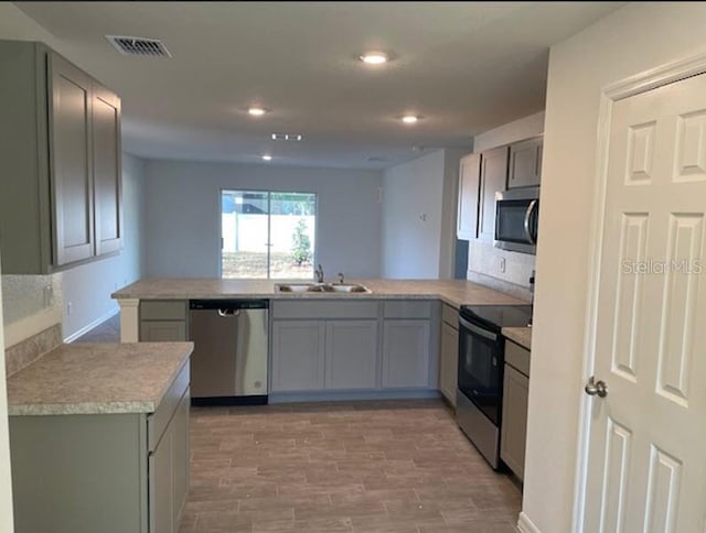 kitchen featuring appliances with stainless steel finishes, sink, light wood-type flooring, and kitchen peninsula