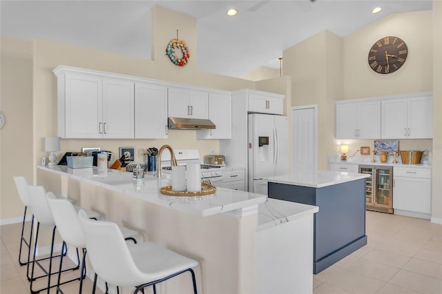 kitchen with white appliances, light tile patterned floors, a kitchen island with sink, and white cabinets