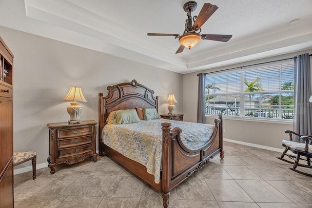 bedroom with light tile patterned flooring, ceiling fan, and a tray ceiling