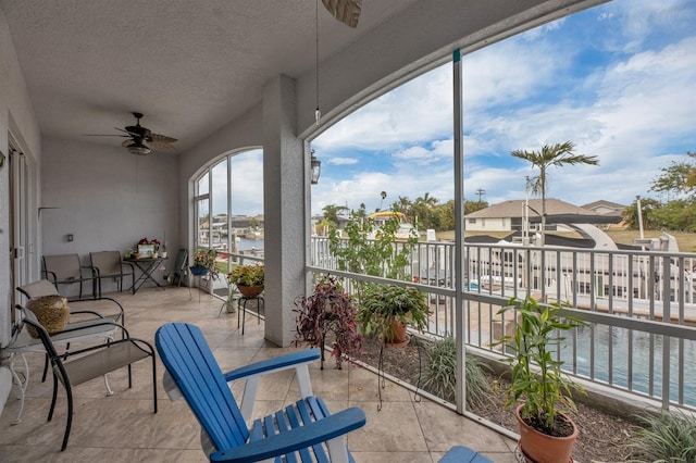 sunroom with ceiling fan and a water view