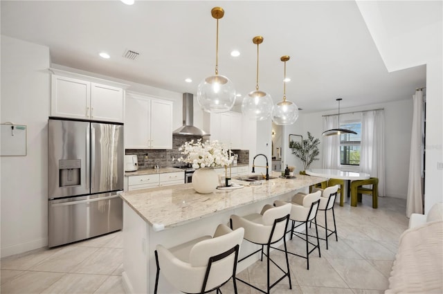 kitchen featuring white cabinets, wall chimney range hood, stainless steel fridge, and hanging light fixtures