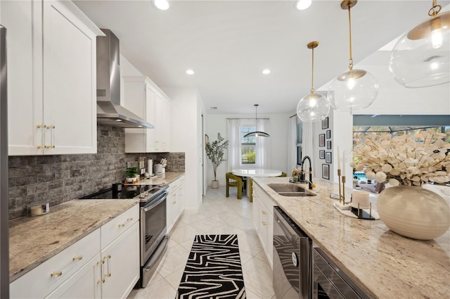 kitchen with appliances with stainless steel finishes, white cabinetry, sink, decorative light fixtures, and wall chimney exhaust hood