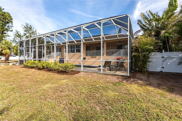 rear view of house with a patio, glass enclosure, and a lawn