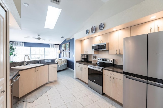 kitchen featuring lofted ceiling with skylight, sink, light tile patterned floors, stainless steel appliances, and light brown cabinets