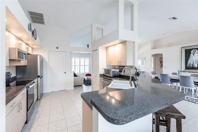 kitchen featuring appliances with stainless steel finishes, a breakfast bar, sink, light tile patterned floors, and kitchen peninsula