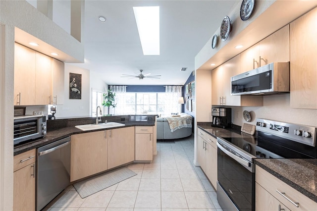 kitchen with sink, appliances with stainless steel finishes, kitchen peninsula, dark stone counters, and light brown cabinets