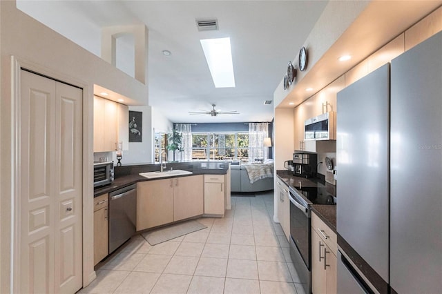 kitchen featuring appliances with stainless steel finishes, a skylight, sink, light tile patterned floors, and kitchen peninsula