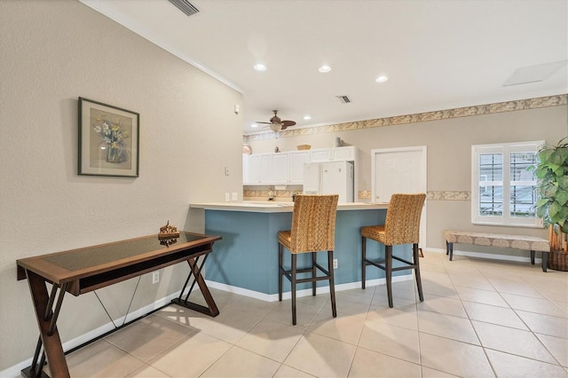 kitchen with light tile patterned floors, a breakfast bar area, white refrigerator with ice dispenser, white cabinets, and kitchen peninsula