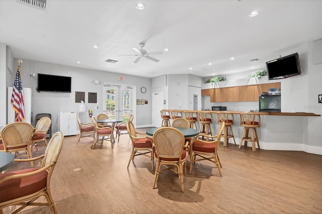 dining space featuring bar, light hardwood / wood-style flooring, ceiling fan, and french doors