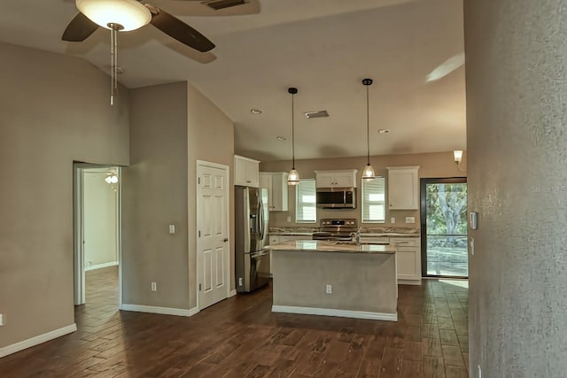 kitchen featuring dark wood-type flooring, appliances with stainless steel finishes, white cabinetry, an island with sink, and decorative light fixtures