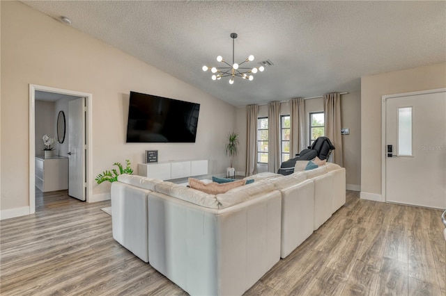 living room with lofted ceiling, a notable chandelier, light hardwood / wood-style floors, and a textured ceiling