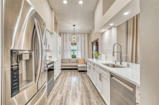 kitchen with pendant lighting, sink, white cabinets, stainless steel appliances, and light hardwood / wood-style flooring