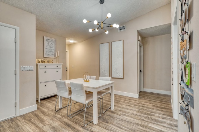 dining room with vaulted ceiling, a notable chandelier, a textured ceiling, and light hardwood / wood-style flooring