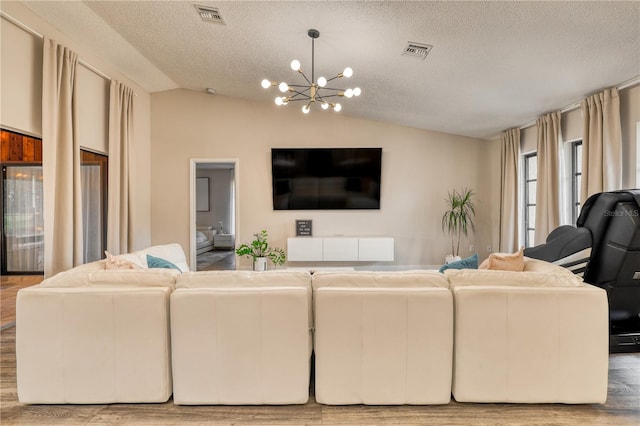 living room with lofted ceiling, a notable chandelier, light hardwood / wood-style flooring, and a textured ceiling