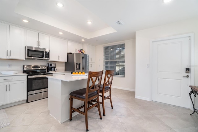 kitchen featuring a breakfast bar area, white cabinetry, appliances with stainless steel finishes, a raised ceiling, and a kitchen island