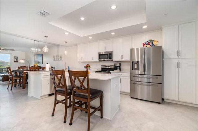 kitchen with hanging light fixtures, a raised ceiling, appliances with stainless steel finishes, and white cabinetry