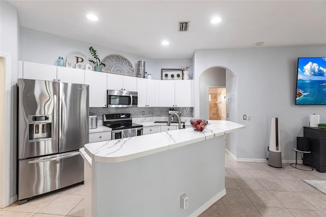 kitchen featuring appliances with stainless steel finishes, white cabinetry, a kitchen island with sink, light tile patterned floors, and decorative backsplash