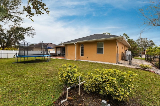 back of house featuring a trampoline and a lawn