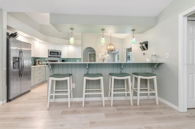 kitchen with kitchen peninsula, appliances with stainless steel finishes, white cabinetry, a kitchen bar, and decorative backsplash