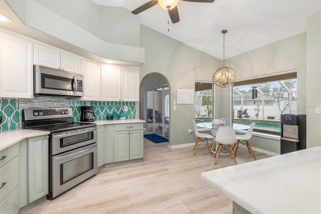 kitchen featuring ceiling fan with notable chandelier, pendant lighting, white cabinets, appliances with stainless steel finishes, and tasteful backsplash