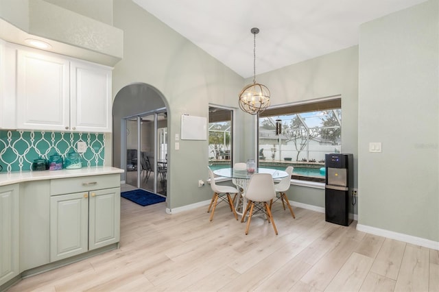 dining space with a notable chandelier, vaulted ceiling, and light hardwood / wood-style flooring