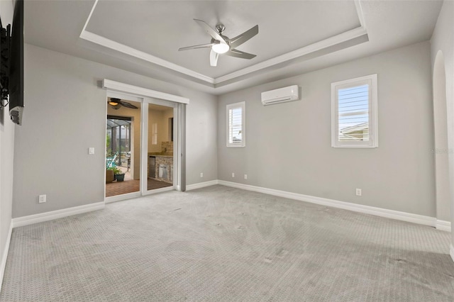 empty room featuring a raised ceiling, ceiling fan, light colored carpet, and a wall unit AC