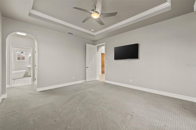 unfurnished bedroom featuring light carpet, a tray ceiling, ensuite bath, and ornamental molding