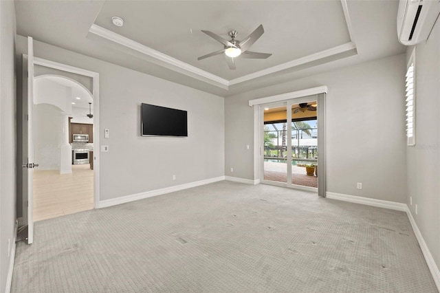 unfurnished room with light carpet, a wall mounted AC, ceiling fan, and a tray ceiling