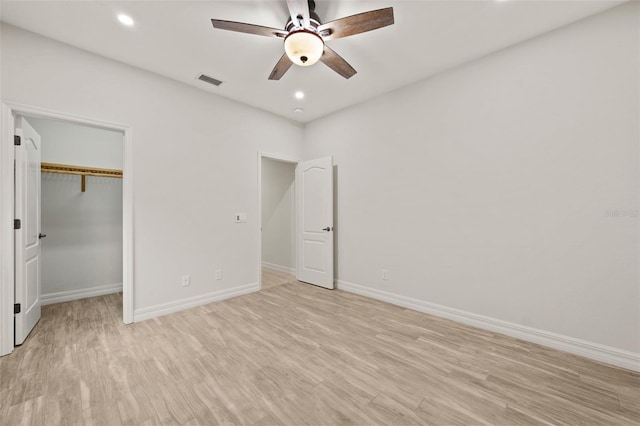 unfurnished bedroom with a closet, a spacious closet, ceiling fan, and light hardwood / wood-style flooring