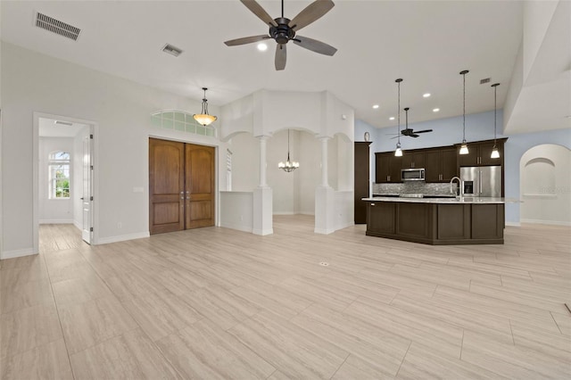 kitchen with ceiling fan with notable chandelier, decorative light fixtures, decorative columns, stainless steel appliances, and a center island with sink