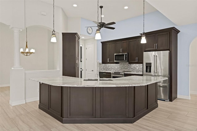 kitchen with sink, light stone counters, pendant lighting, stainless steel appliances, and decorative columns