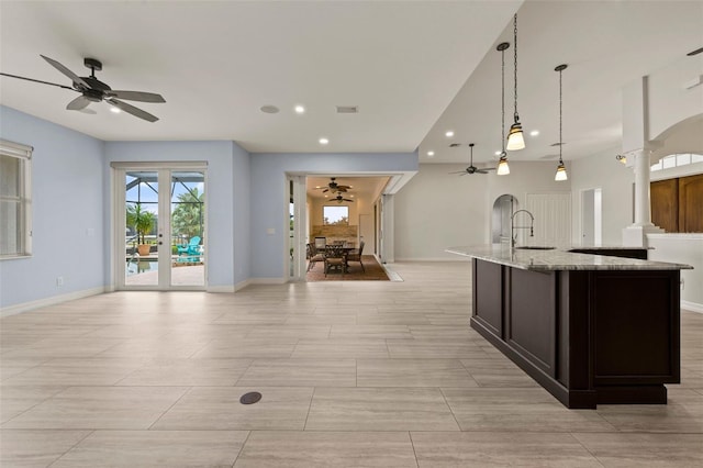 kitchen with sink, light stone counters, hanging light fixtures, ceiling fan, and decorative columns