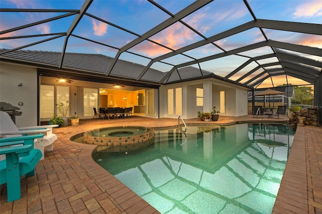 pool at dusk featuring a lanai, a patio, ceiling fan, and an in ground hot tub