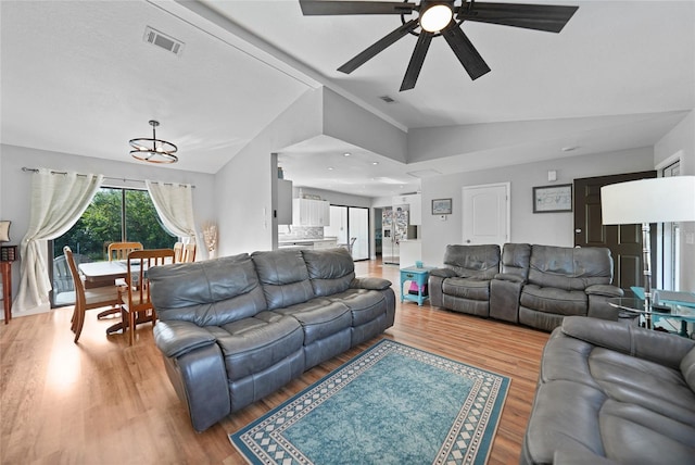 living room with ceiling fan with notable chandelier, wood-type flooring, and vaulted ceiling