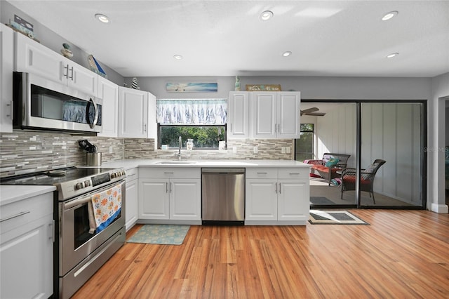 kitchen with sink, white cabinetry, light wood-type flooring, stainless steel appliances, and backsplash