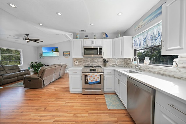 kitchen featuring stainless steel appliances, vaulted ceiling, sink, and white cabinets