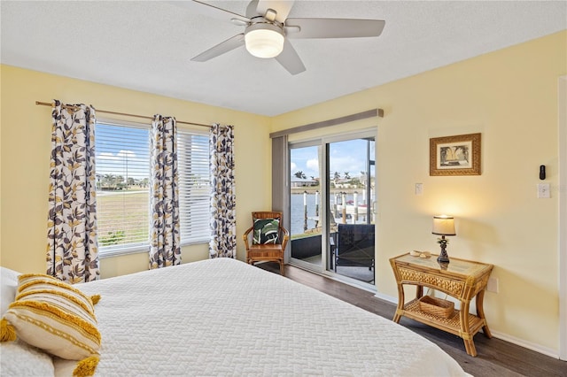 bedroom with a textured ceiling, dark hardwood / wood-style flooring, access to outside, a water view, and ceiling fan